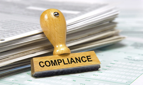 a stack of documents on a table with a compliance stamp beside it signifying Compliance